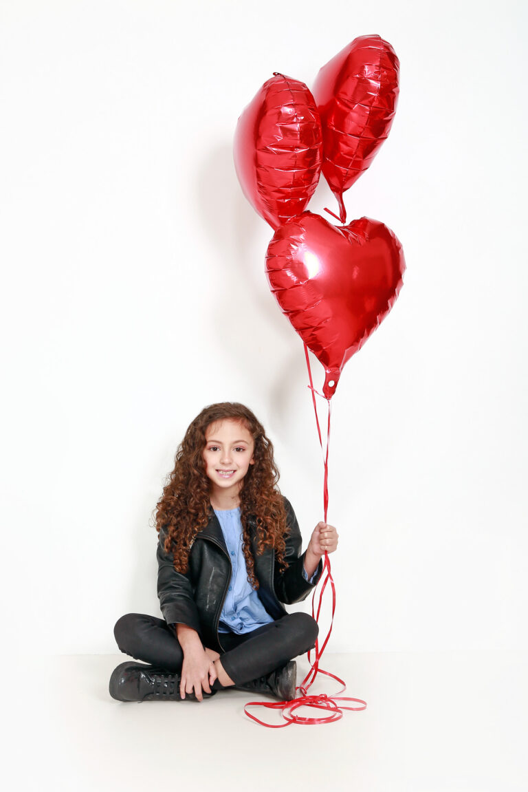 Photo couleur d'une enfant brune avec des ballon en forme de coeur.