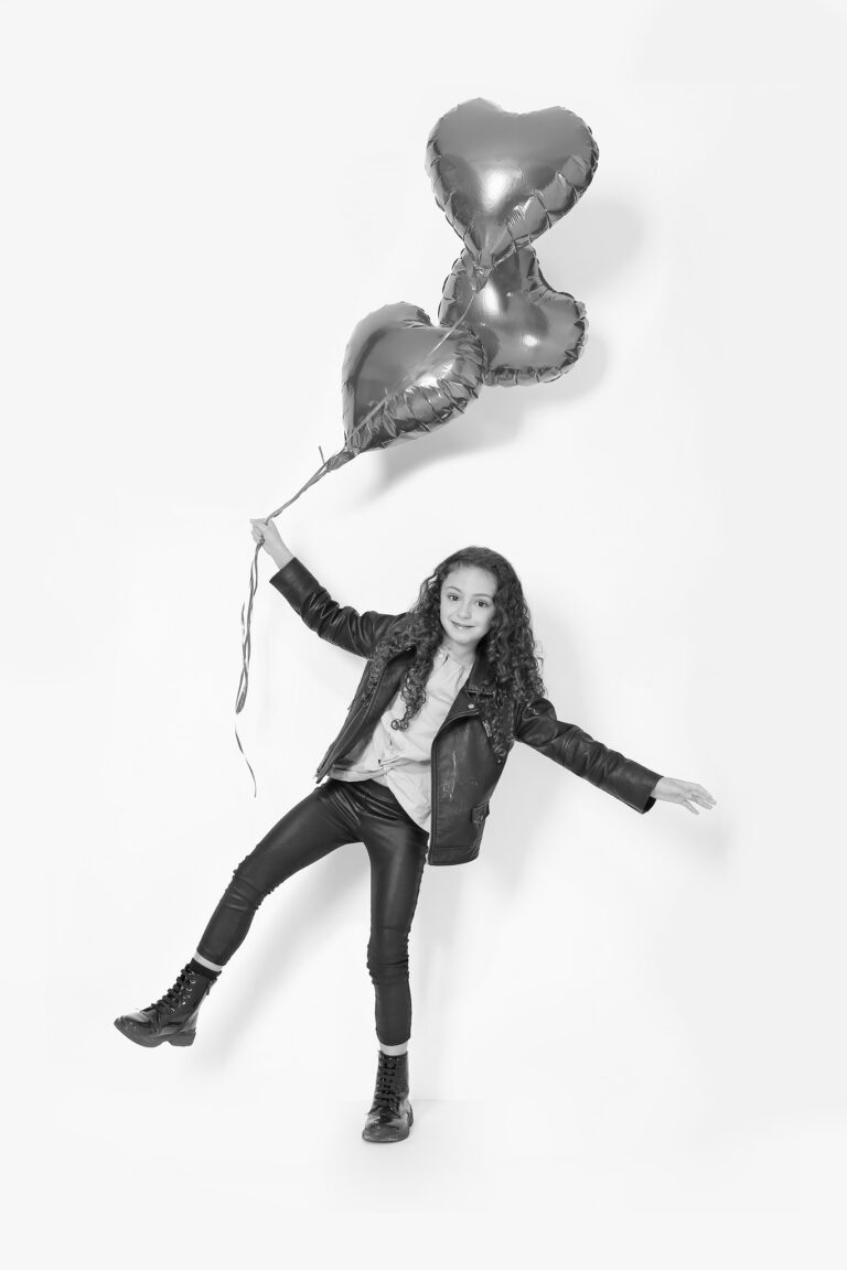 Photo noire et blanc d'une enfant brune avec des ballon en forme de coeur.