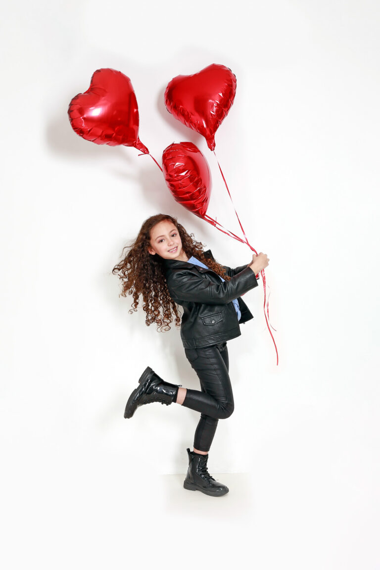 Photo couleur d'une enfant brune avec des ballon en forme de coeur.